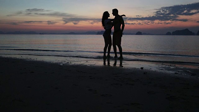 一对情侣在海滩上亲吻在日落，男人和女人在水里牵手拥抱