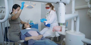 开始牙科治疗，医生放下牙科椅。牙医打开灯，女张开嘴