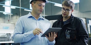 安全帽工程师和工厂工人正在生产设备上使用平板电脑