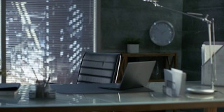 现代办公室的镜头与皮革椅子，木材和玻璃桌子上的笔记本电脑。工作空间是黑暗的色彩，大都市是透过窗户看到的。
