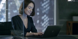 一位女性高管在她的私人办公室里用笔记本电脑工作。她笑着迷人。她的工作空间是在黑暗的基调。