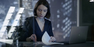 美丽的女执行官在她的私人办公室里签署重要的商业文件。她的身后是一扇可以看到大城市风景的窗户。