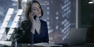在她的私人办公室里，有魅力的女经理正坐在她的桌子旁讲电话。她的身后是一扇可以看到大城市风景的窗户。