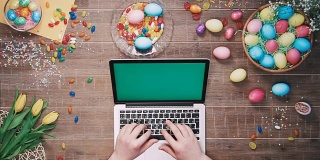人用绿色屏幕的笔记本电脑在装饰复活节彩蛋的桌子上俯视图