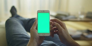 一名男子躺在家里的沙发上，用绿色屏幕竖屏打电话。