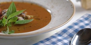 配以罗勒叶和圣女果装饰的海鲜番茄汤，用白色盘子盛在桌上。