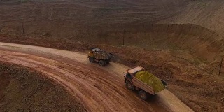 两辆自动倾卸卡车将矿石从采石场运出。矿井全景图。新月形沙丘砂。矿产资源的开发。
