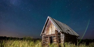 时间流逝的星空在森林边缘与木屋木屋在前景在夏季。
