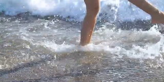 海滩上晒黑的女性腿。海水在沙滩上溅在脚上
