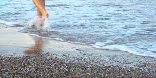 女人美丽的晒黑的腿走在沙滩上。走在海上的女孩