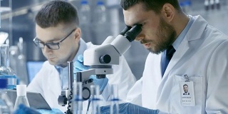 在一个现代实验室里，两位科学家进行实验。首席研究科学家告诉他的助手他在显微镜下看到的结果。