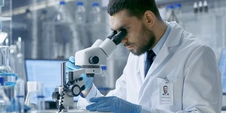 研究科学家用手术钳调整培养皿中的样本，并在显微镜下观察。他在一家现代化实验室工作。