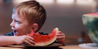 可爱的小男孩看着镜头，吃着西瓜，笑着。快乐男捧着一片，欢呼着