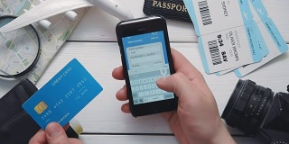 俯视图旅客的手支付机票在线使用智能手机在白色木制桌子