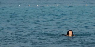 一个留着长发的年轻女子在阳光灿烂的日子里在海里游泳