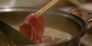 女人用筷子把滑猪肉放进火锅里的特写镜头