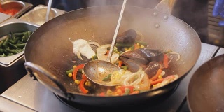 在街头美食节上，专业厨师正在用蔬菜煎贻贝和虾。烤虾和软体动物近距离。海鲜的烹调过程。传统的亚洲食物