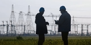 两名工程师戴着安全帽在一个能源站检查期间用智能手机聊天。