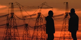 在一个能源变电站检查期间，两个工程师戴着安全帽积极地讨论在红色日落。