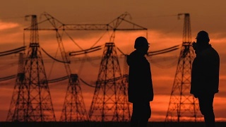 在一个能源变电站检查期间，两个工程师戴着安全帽积极地讨论在红色日落。视频素材模板下载