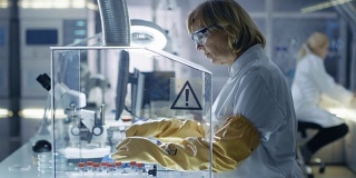 高级女性生物学家在隔离手套箱中处理样本。她在一个现代化，繁忙的实验室配备了最先进的技术。