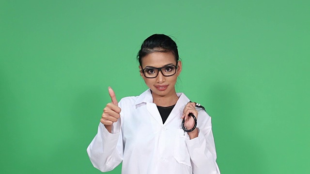 女亚裔皮肤黝黑医生与眼镜，听诊器，转身微笑和拇指欢呼