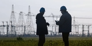 两名工程师戴着安全帽在一个能源站检查期间用智能手机聊天。