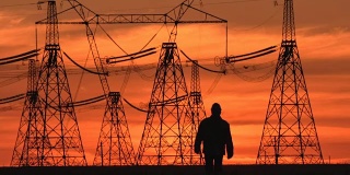 在一个能源变电所检查期间，在红色日落沿着电力线的主管剪影的广泛镜头。