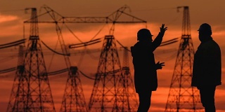 在一个能源变电站检查期间，两个工程师戴着安全帽积极地讨论在红色日落。