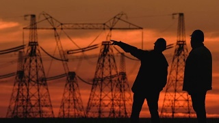 在一个能源变电站检查期间，两个工程师戴着安全帽积极地讨论在红色日落。视频素材模板下载