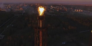 夕阳西下时，树林中炼油厂上的一座塔上挂着火炬。鸟瞰图