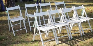 婚礼设置在花园，公园。外面举行婚礼，庆祝。婚礼的殿堂的装饰。婚礼前，草坪上放着一排排的白色木制空椅子。缓慢的锅