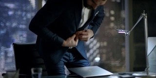 一名商人解开夹克，坐在办公桌前，开始在笔记本电脑上打字。他的办公室可以俯瞰整个大城市。