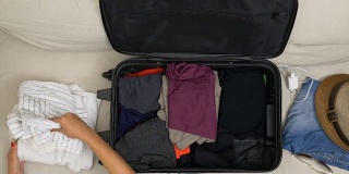 俯视图女人的手与红色指甲填充手提箱与折叠的衣服旅行旅行