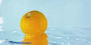 一个橙子落在闪亮的水面上的慢动作镜头