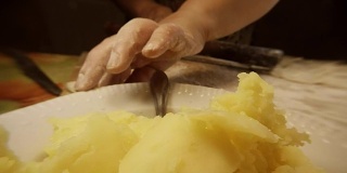 女人手后装土豆的盘子，用擀面杖把过去的土豆卷起来，用面粉煮