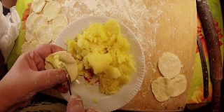 桌上的盘子上有煮土豆，面团和面粉，手模具Varenik俯视图