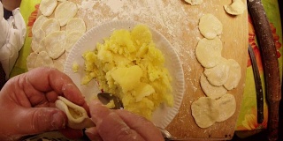 女人用勺子从盘子里拿土豆，把它放进面团和模具里三个瓦伦尼克