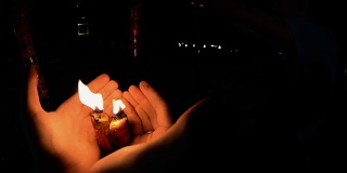 晚上在佛寺里点燃蜡烛。男人的手在火红的大蜡烛在寺庙gopro。中国庙里的红烛。第一人称射击。泰国的寺庙