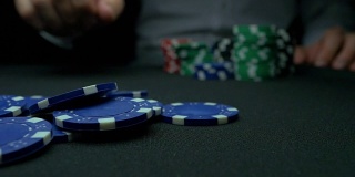 在黑色背景下，男人的手从扑克桌上拿走筹码。筹码和手放在绿色桌上。“手”用慢动作拿走扑克中的赢钱