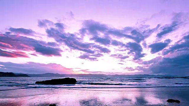 乌云密布的天空在夕阳的最后余晖下，在海面和科门德尔山脉上呈现出粉红色