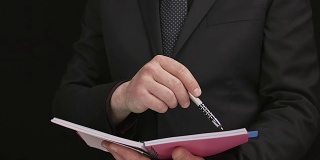 穿着黑色西装和蓝色领带的商人拿着一个记录笔记本评估合同数据
