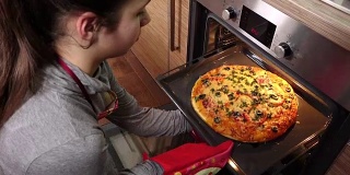 女孩从烤箱里拿出热披萨