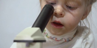 一个小女孩在一堵白墙旁边玩显微镜。