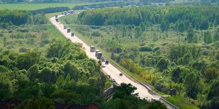 许多卡车和汽车在树林和田野之间的一条长长的道路上行驶。间隔拍摄