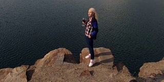 女孩在湖边的悬崖边喝酒。