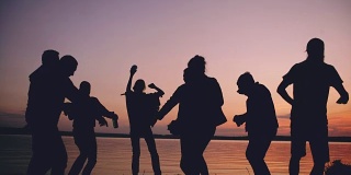 日落时分，一群跳舞的年轻人在海滩上举行聚会