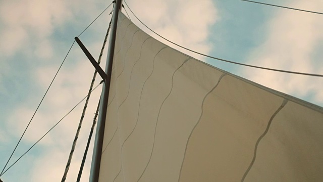 在多云的夏日天空的背景下，游艇的船帆摇曳着