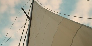 在多云的夏日天空的背景下，游艇的船帆摇曳着
