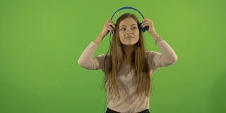 一位年轻漂亮的白人模特戴着耳机听音乐，跳舞。在绿色的背景上。